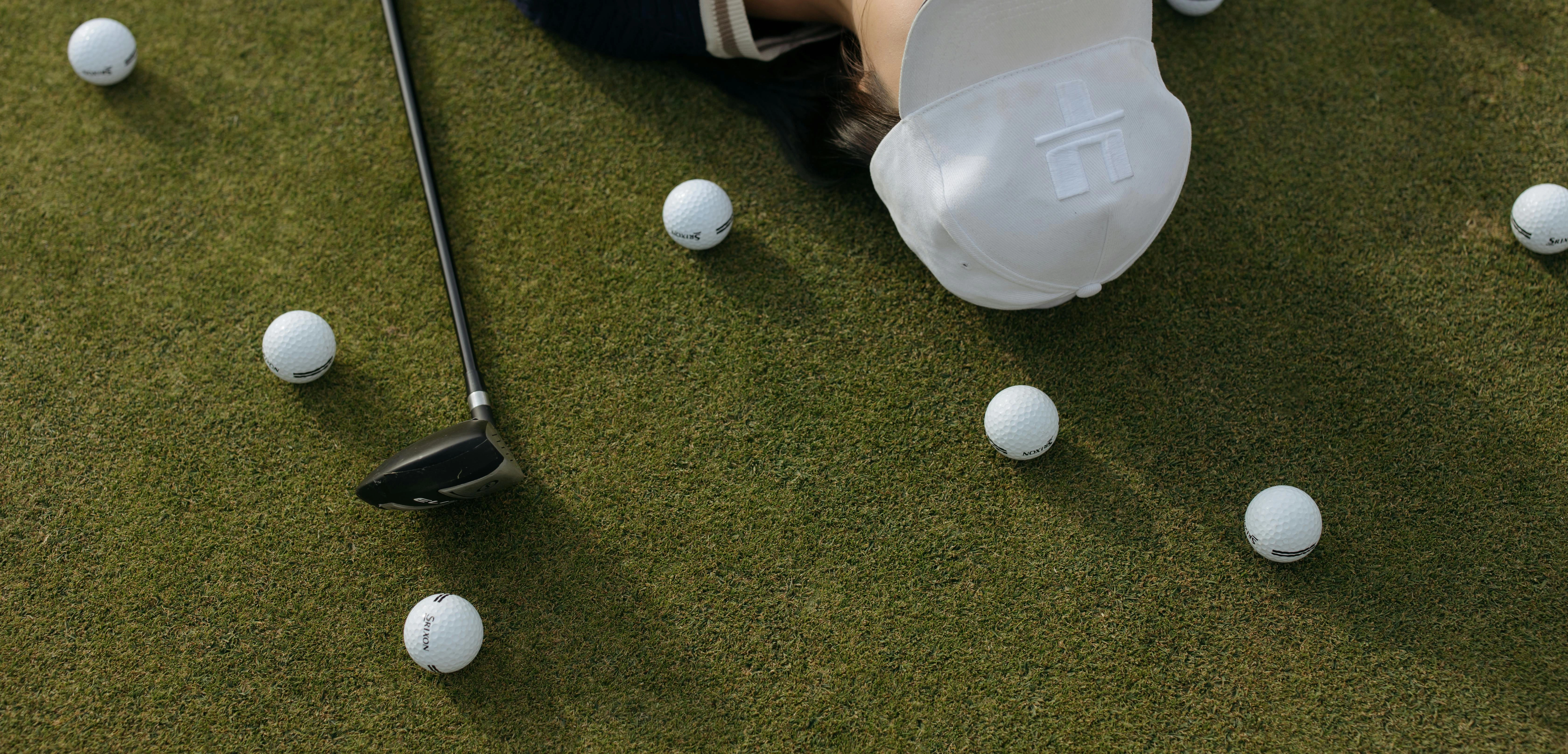 Golferin liegt am Boden. Golfbälle liegen daneben.