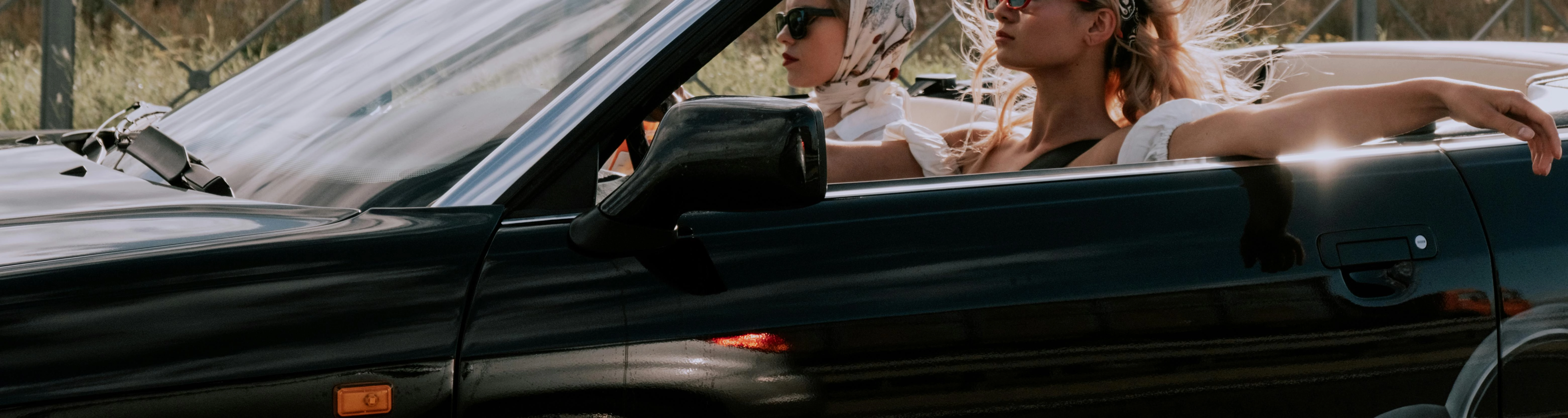 Two women driving in a convertible car.